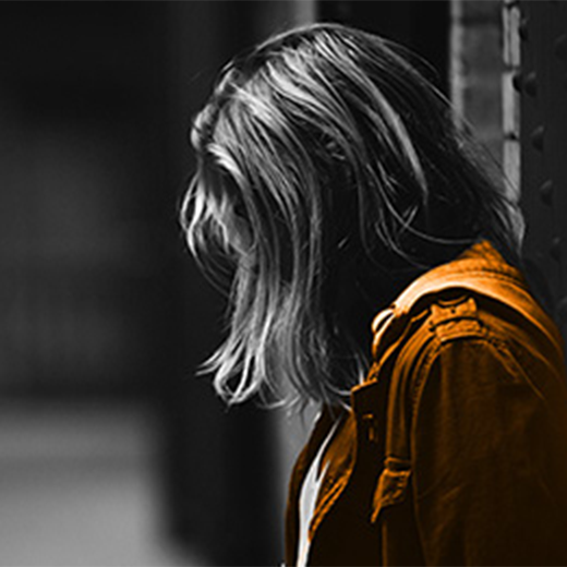 Black and white photo of side profile of a girl in an alley looking down with her jacket coloured orange